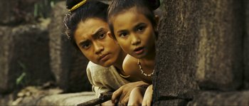 Movie still from “Ong Bak 2” (2008), directed by Tony Jaa – Two young people pose for a picture while leaning against a tree; Medium shot, High angle