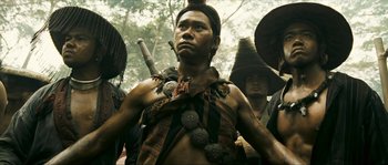 Movie still from “Ong Bak 2” (2008), directed by Tony Jaa – A man in a native american costume with other men; Medium shot, Low angle