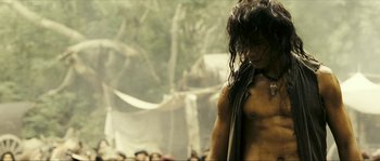 Movie still from “Ong Bak 2” (2008), directed by Tony Jaa – A shirtless man standing in front of a group of people; Medium shot, Low angle