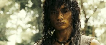 Movie still from “Ong Bak 2” (2008), directed by Tony Jaa – A man with long black hair wearing a necklace; Close Up shot, Low angle