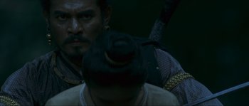 Movie still from “Ong Bak 2” (2008), directed by Tony Jaa – A man's face with a hat on his head; Close Up shot, Over the shoulder angle