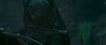 Movie still from “Ong Bak 2” (2008), directed by Tony Jaa – A person in a black outfit and a black mask; Medium shot, Low angle