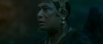 Movie still from “Ong Bak 2” (2008), directed by Tony Jaa – A man with a gold head dress and a black shirt; Close Up shot, Low angle