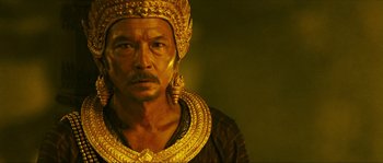 Movie still from “Ong Bak 2” (2008), directed by Tony Jaa – A man wearing a gold headdress and a black shirt; Close Up shot, Low angle