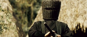 Movie still from “Ong Bak 2” (2008), directed by Tony Jaa – A person with a mask holding a sword in front of their face; Close Up shot, Low angle