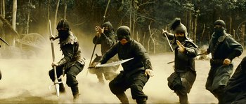 Movie still from “Ong Bak 2” (2008), directed by Tony Jaa – A group of men in black suits and masks holding swords; Wide shot, High angle