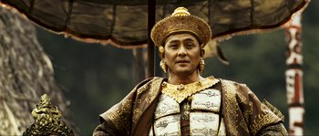 Movie still from “Ong Bak 2” (2008), directed by Tony Jaa – A man wearing a gold hat and a brown and gold outfit; Close Up shot, Low angle