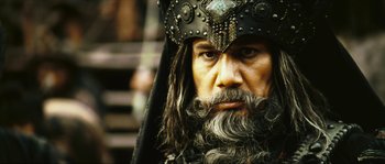 Movie still from “Ong Bak 2” (2008), directed by Tony Jaa – A man with long hair and a beard wearing a hat; Close Up shot, Low angle