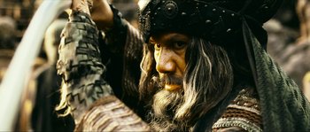 Movie still from “Ong Bak 2” (2008), directed by Tony Jaa – A person with a beard wearing a helmet; Close Up shot, Low angle