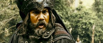 Movie still from “Ong Bak 2” (2008), directed by Tony Jaa – A person with a beard wearing a helmet; Close Up shot, Low angle