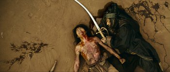 Movie still from “Ong Bak 2” (2008), directed by Tony Jaa – A man is laying on the ground holding a sword; Medium shot, Overhead angle