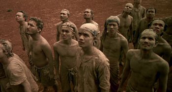 Movie still from “Ong-Bak: The Thai Warrior” (2003), directed by Prachya Pinkaew – A group of young men standing in a dirt field; Wide shot, High angle