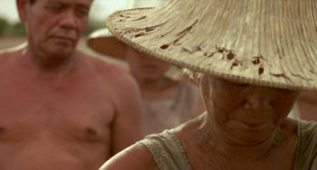 Movie still from “Ong-Bak: The Thai Warrior” (2003), directed by Prachya Pinkaew – An older woman wearing a straw hat with two other people in the background; Close Up shot, Low angle