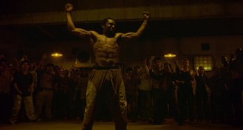Movie still from “Ong-Bak: The Thai Warrior” (2003), directed by Prachya Pinkaew – A man with no shirt is standing in front of a crowd of onlookers; Wide shot, Low angle