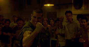 Movie still from “Ong-Bak: The Thai Warrior” (2003), directed by Prachya Pinkaew – A group of people in a room with a man with a fist in the air; Close Up shot, Low angle