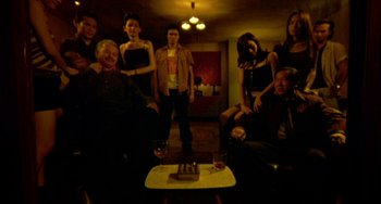 Movie still from “Ong-Bak: The Thai Warrior” (2003), directed by Prachya Pinkaew – A group of people standing around a table with a cake on it; Wide shot, High angle