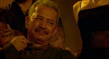 Movie still from “Ong-Bak: The Thai Warrior” (2003), directed by Prachya Pinkaew – A person sitting in a chair; Close Up shot, Over the shoulder angle