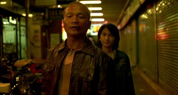 Movie still from “Ong-Bak: The Thai Warrior” (2003), directed by Prachya Pinkaew – A man and a woman are standing in a hallway; Medium shot, Low angle