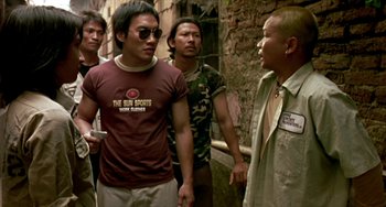 Movie still from “Ong-Bak: The Thai Warrior” (2003), directed by Prachya Pinkaew – A group of men standing next to each other on a street; Medium shot, Low angle
