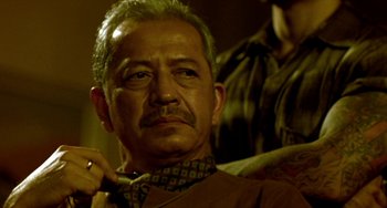 Movie still from “Ong-Bak: The Thai Warrior” (2003), directed by Prachya Pinkaew – An older man with a goatee is holding a pipe; Close Up shot, Low angle