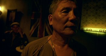 Movie still from “Ong-Bak: The Thai Warrior” (2003), directed by Prachya Pinkaew – An older man wearing a necklace in a dark room; Close Up shot, Low angle