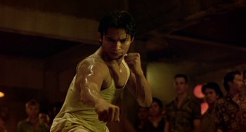 Movie still from “Ong-Bak: The Thai Warrior” (2003), directed by Prachya Pinkaew – A man in a white tank top is boxing; Close Up shot, Low angle