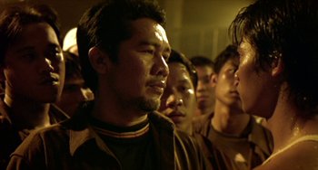 Movie still from “Ong-Bak: The Thai Warrior” (2003), directed by Prachya Pinkaew – A group of men standing next to each other in a room; Close Up shot, Over the shoulder angle