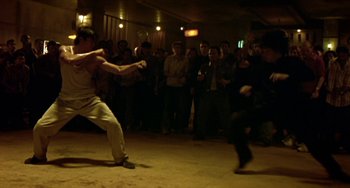 Movie still from “Ong-Bak: The Thai Warrior” (2003), directed by Prachya Pinkaew – A group of people in a room watching a man kick a ball; Wide shot, High angle