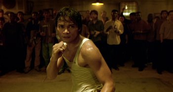 Movie still from “Ong-Bak: The Thai Warrior” (2003), directed by Prachya Pinkaew – A man in a white tank top is in a crowd; Close Up shot, High angle