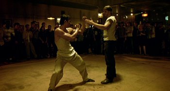 Movie still from “Ong-Bak: The Thai Warrior” (2003), directed by Prachya Pinkaew – Two men are practicing martial arts in an indoor setting; Wide shot, High angle