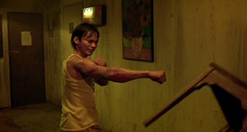 Movie still from “Ong-Bak: The Thai Warrior” (2003), directed by Prachya Pinkaew – A man in a tan shirt is boxing in a room; Medium shot, Over the shoulder angle