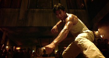 Movie still from “Ong-Bak: The Thai Warrior” (2003), directed by Prachya Pinkaew – A man in a white shirt and brown pants is fighting; Medium shot, Low angle