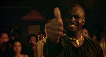 Movie still from “Ong-Bak: The Thai Warrior” (2003), directed by Prachya Pinkaew – A man giving a thumbs up at a party; Close Up shot, Low angle