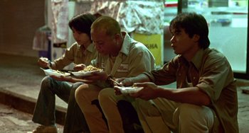 Movie still from “Ong-Bak: The Thai Warrior” (2003), directed by Prachya Pinkaew – A group of people sitting down eating food; Wide shot, High angle
