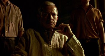 Movie still from “Ong-Bak: The Thai Warrior” (2003), directed by Prachya Pinkaew – An older man is holding a cell phone in his hand; Medium shot, Low angle