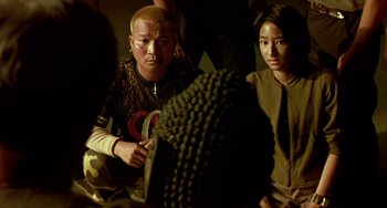 Movie still from “Ong-Bak: The Thai Warrior” (2003), directed by Prachya Pinkaew – A man and a woman sitting next to each other in a room; Medium shot, Over the shoulder angle