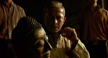 Movie still from “Ong-Bak: The Thai Warrior” (2003), directed by Prachya Pinkaew – An older man is holding a mask in his hand; Close Up shot, Low angle