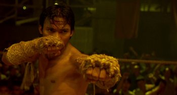 Movie still from “Ong-Bak: The Thai Warrior” (2003), directed by Prachya Pinkaew – A shirtless man with a pair of hairy hands in front of his face; Close Up shot, Low angle