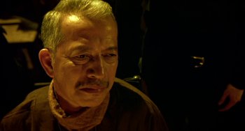 Movie still from “Ong-Bak: The Thai Warrior” (2003), directed by Prachya Pinkaew – An older man with a mustache is looking at the camera; Close Up shot, Low angle