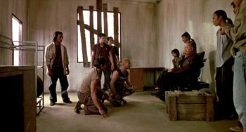 Movie still from “Ong-Bak: The Thai Warrior” (2003), directed by Prachya Pinkaew – A group of people standing around in a room; Wide shot, Over the shoulder angle