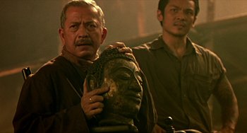 Movie still from “Ong-Bak: The Thai Warrior” (2003), directed by Prachya Pinkaew – A man holding a buddha statue in front of another man; Close Up shot, Over the shoulder angle