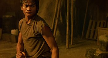 Movie still from “Ong-Bak: The Thai Warrior” (2003), directed by Prachya Pinkaew – A young man is standing in front of a wall; Medium shot, Low angle