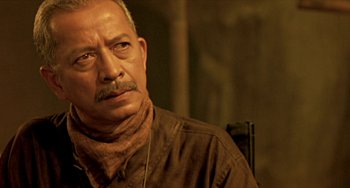 Movie still from “Ong-Bak: The Thai Warrior” (2003), directed by Prachya Pinkaew – An older man wearing a neck scarf looking at the camera; Close Up shot, Over the shoulder angle