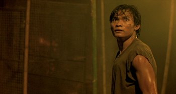 Movie still from “Ong-Bak: The Thai Warrior” (2003), directed by Prachya Pinkaew – A man standing in the dark looking at the camera; Close Up shot, Low angle