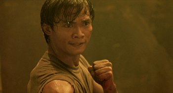 Movie still from “Ong-Bak: The Thai Warrior” (2003), directed by Prachya Pinkaew – A young man is holding his fist up to his face; Close Up shot, High angle