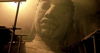 Movie still from “Ong-Bak: The Thai Warrior” (2003), directed by Prachya Pinkaew – A large statue of a person in a room with sunlight coming through the window; Wide shot, Low angle