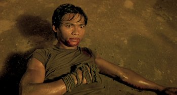 Movie still from “Ong-Bak: The Thai Warrior” (2003), directed by Prachya Pinkaew – A man with blood all over his face and hands tied up; Medium shot, Overhead angle