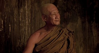 Movie still from “Ong-Bak: The Thai Warrior” (2003), directed by Prachya Pinkaew – An older man wearing a brown robe is looking at the camera; Close Up shot, Low angle