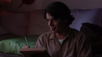 Movie still from “Open Your Eyes” (1997), directed by Alejandro Amenábar – A man sitting in front of an open book with a pen in his mouth; Medium shot, Low angle