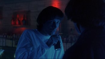 Movie still from “Open Your Eyes” (1997), directed by Alejandro Amenábar – A young man holding a drink in his hand while standing next to another man; Medium shot, Over the shoulder angle